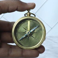 Close-up of the brass compass dial held in hand, showing the detailed markings and magnetized needle.