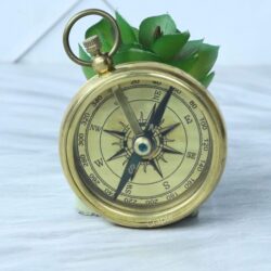A three-quarter view of the open-face brass pocket compass, displaying its antique-style dial and top loop.