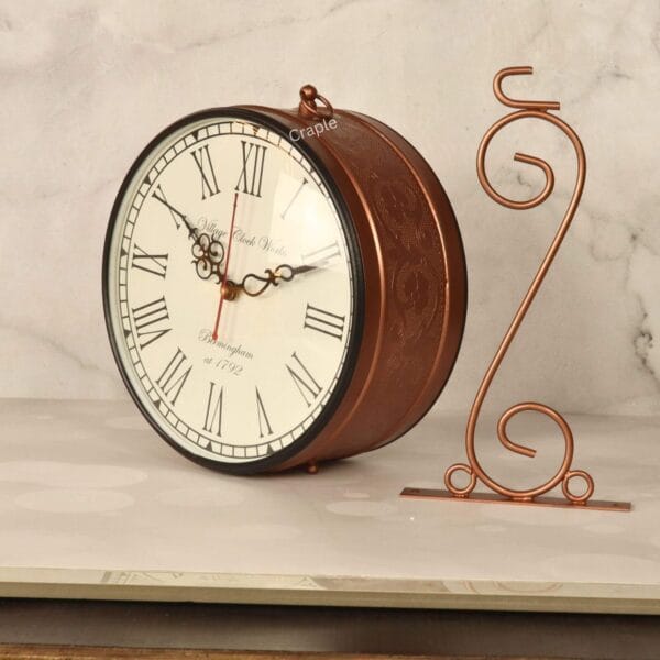 Double-sided vintage station clock displayed on a decorative brass-coated tabletop stand with a swirl design.