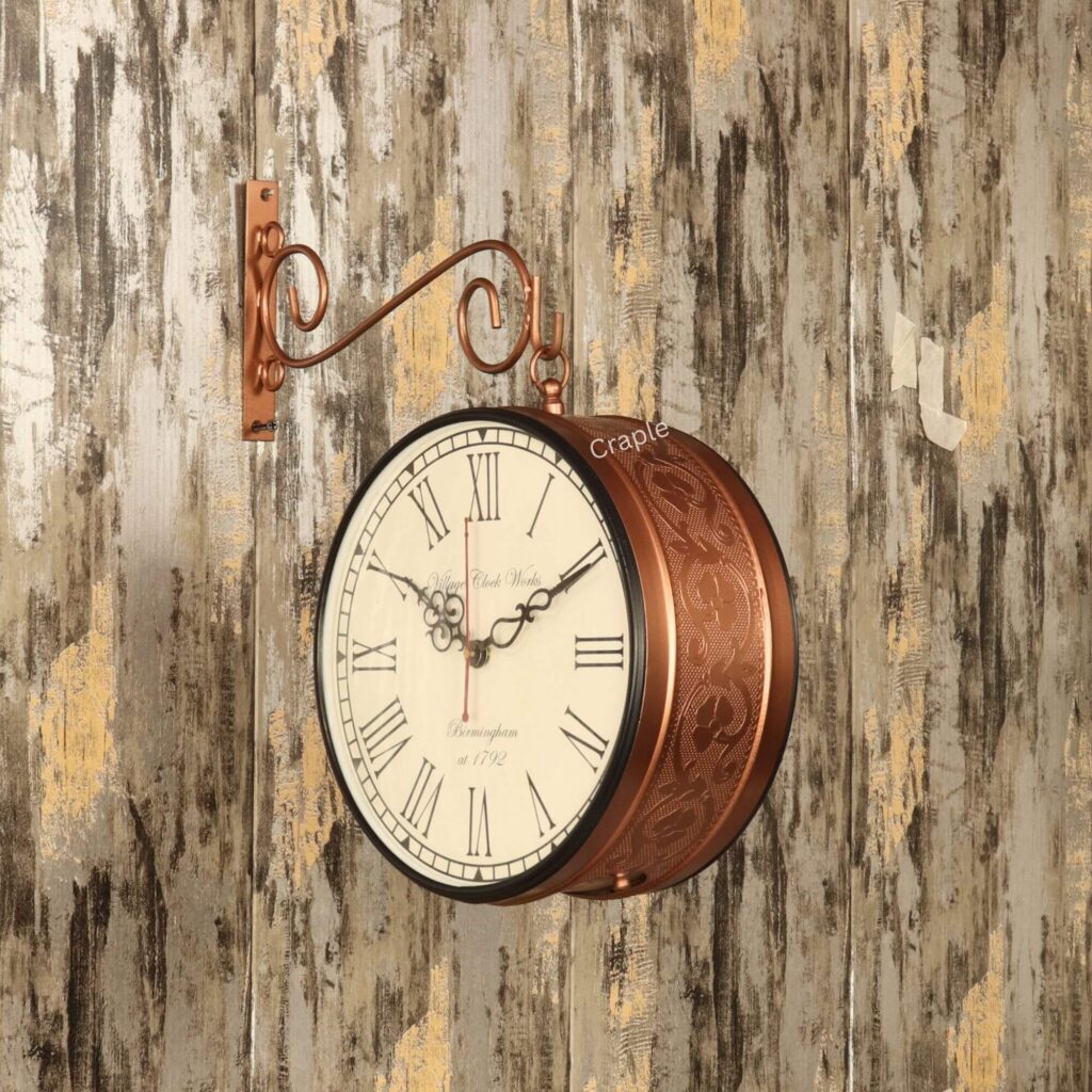 Antique-style double-sided station clock with an embossed brass case, hanging from a decorative scroll bracket on a rustic wall.