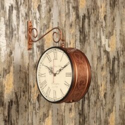Antique-style double-sided station clock with an embossed brass case, hanging from a decorative scroll bracket on a rustic wall.