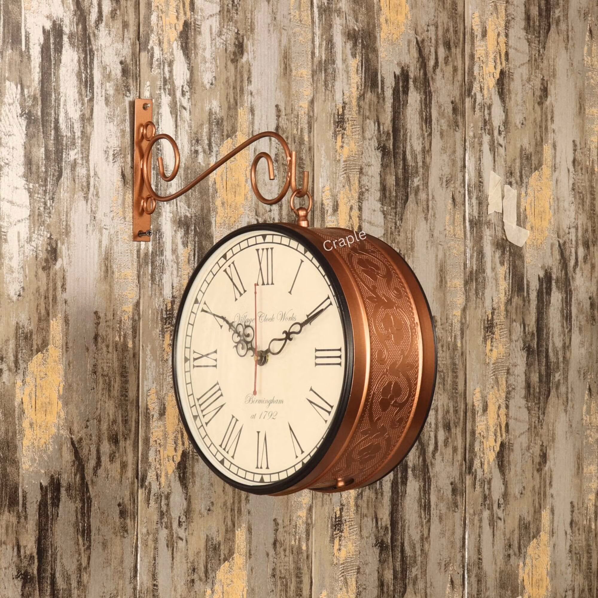 Embossed Double-Sided Steel Station Clock-3 Antique-style double-sided station clock with an embossed brass case, hanging from a decorative scroll bracket on a rustic wall.