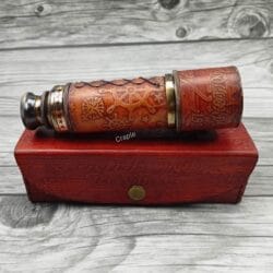 Vintage brass telescope wrapped in embossed leather, shown in its collapsed form resting on top of its red leather storage box.