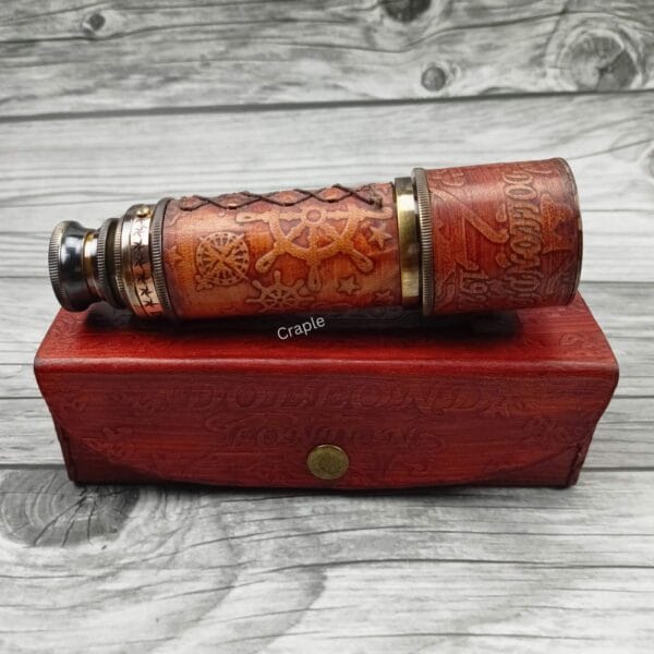 Vintage brass telescope wrapped in embossed leather, shown in its collapsed form resting on top of its red leather storage box.
