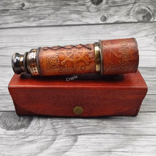 Vintage brass telescope wrapped in embossed leather, shown in its collapsed form resting on top of its red leather storage box.
