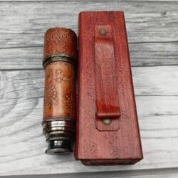 Collapsible brass and leather telescope shown beside its embossed red leather travel case, highlighting the portability.