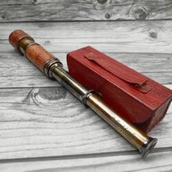 Nautical-style extendable brass telescope with a detailed embossed leather grip, shown with its red case.