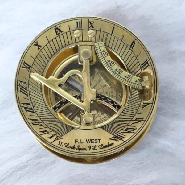 Top-down view of a shiny brass F.L. West London sundial compass showing the gnomon, latitude scale, and Roman numerals.