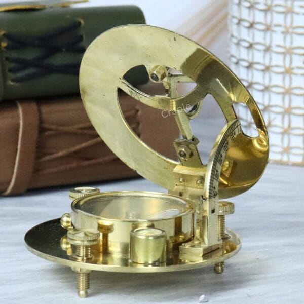 Brass sundial with its top ring opened, revealing the internal magnetic compass needle and cardinal points.