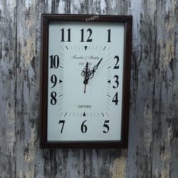 Front view of a rectangular wooden wall clock with a white face, large Arabic numerals, and ornate hands.