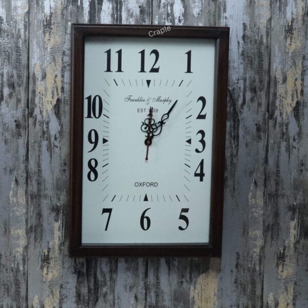 Front view of a rectangular wooden wall clock with a white face, large Arabic numerals, and ornate hands.