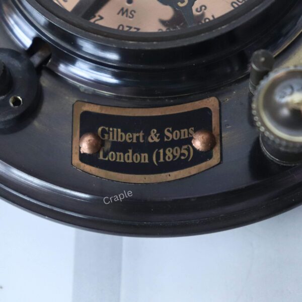 Close-up of the brass plaque engraved with "Gilbert & Sons, London (1895)" on the antique sundial compass.