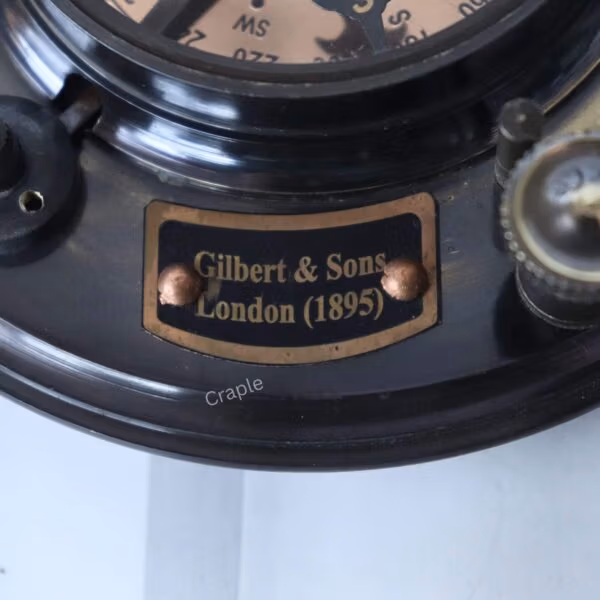 Close-up of the brass plaque engraved with "Gilbert & Sons, London (1895)" on the antique sundial compass.