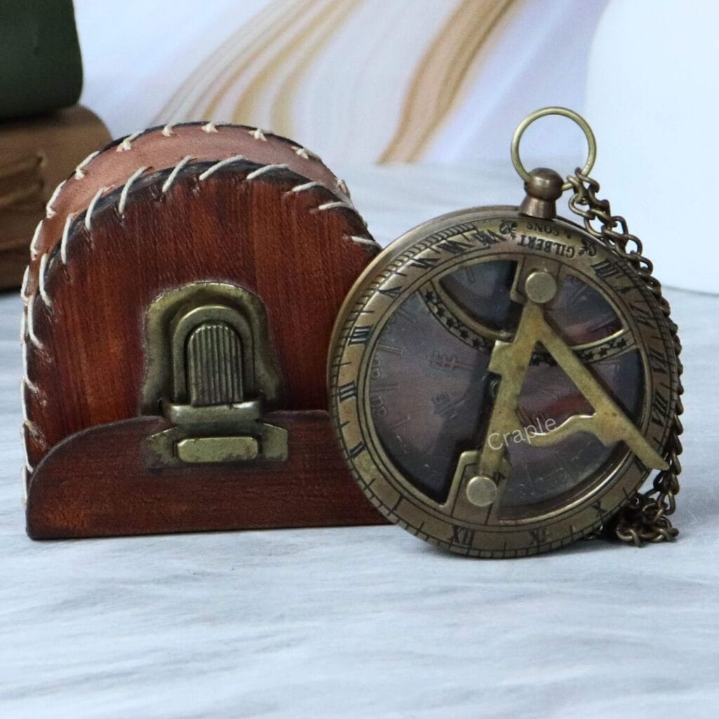 Gilbert & Sons antique brass pocket sundial compass displayed next to its protective, stitched brown leather case.