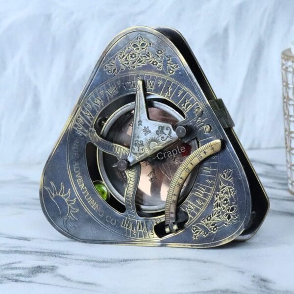 Vintage-style triangular brass sundial compass with a black antique finish, featuring detailed engravings and a foldable gnomon.
