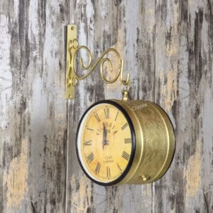 Vintage double-sided station clock with a golden finish, mounted on a rustic wall with its ornate scroll bracket.