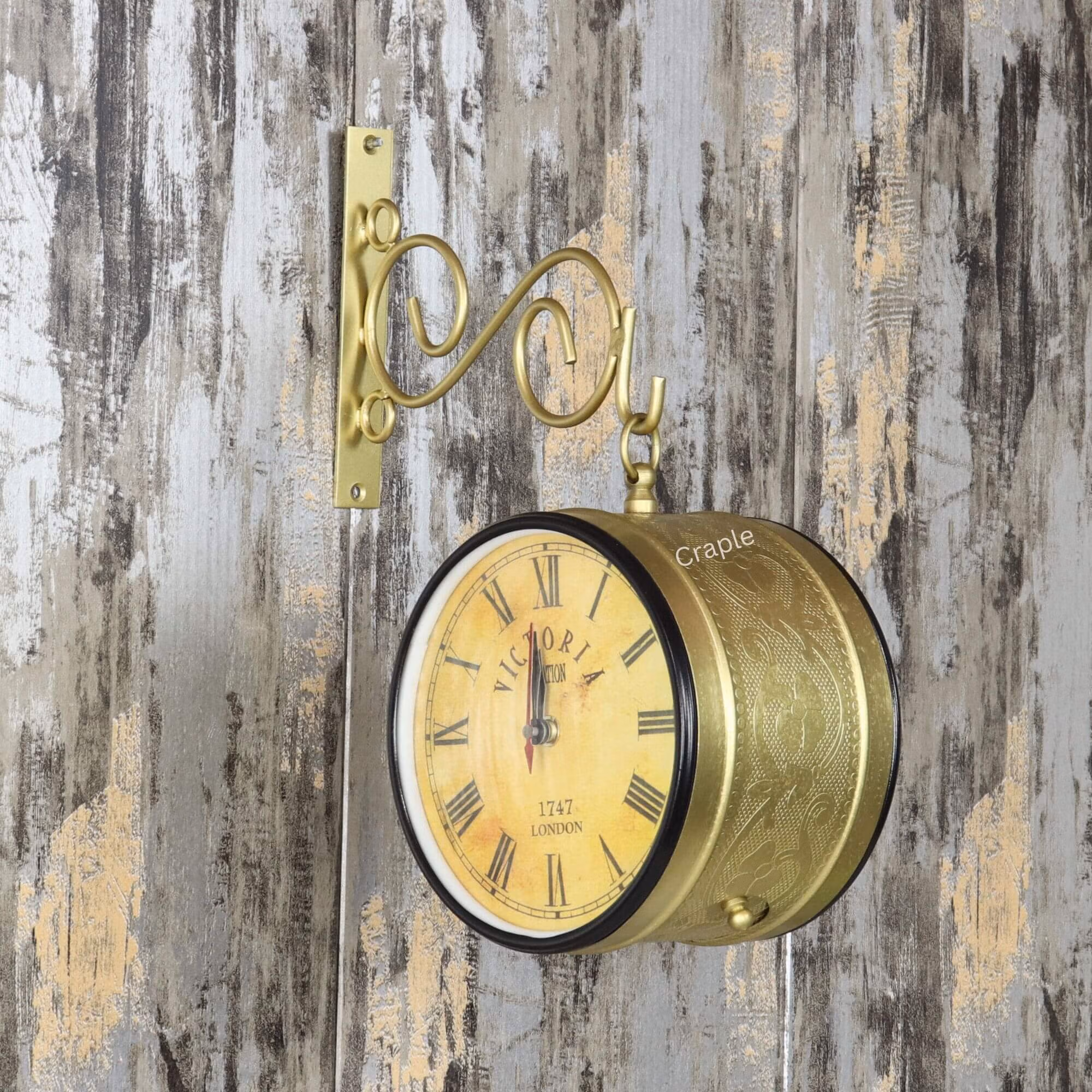 Golden Brass Coated Double-Sided Steel Station Clock-3 Vintage double-sided station clock with a golden finish, mounted on a rustic wall with its ornate scroll bracket.