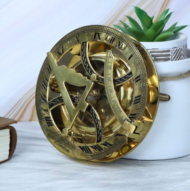 Handcrafted brass sundial compass with a shiny finish, displayed as a decorative piece next to a succulent plant.