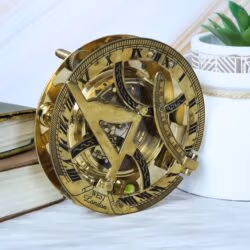 Vintage-style polished brass sundial compass shown as a decorative accessory on a desk next to old books.
