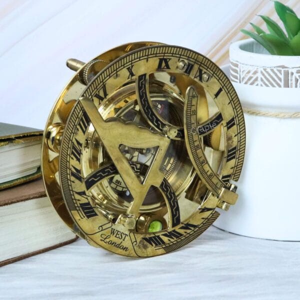 Vintage-style polished brass sundial compass shown as a decorative accessory on a desk next to old books.