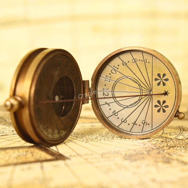 Close-up of the internal sundial dial on the antique brass compass, showing the hour markings and string gnomon.