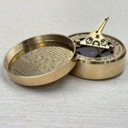 Vintage-style brass pocket sundial with its gnomon raised, revealing the magnetic compass beneath.
