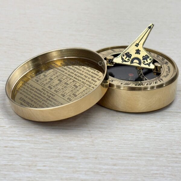 Vintage-style brass pocket sundial with its gnomon raised, revealing the magnetic compass beneath.