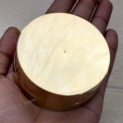 The polished, plain bottom of the brass sundial compass being held in a person's hand.