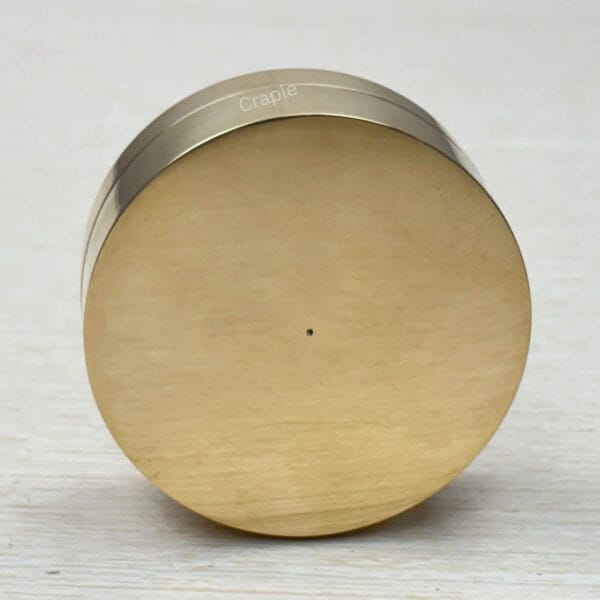 The smooth, un-engraved bottom of the round brass sundial compass case.