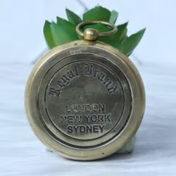 The engraved back of the brass pocket compass showing the "Regal Brand" logo and the words "London, New York, Sydney".