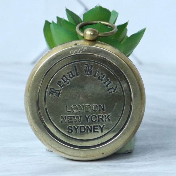 The engraved back of the brass pocket compass showing the "Regal Brand" logo and the words "London, New York, Sydney".
