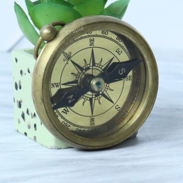 Angled view of the antique-style brass compass, highlighting the shiny finish on its casing and the detailed dial.
