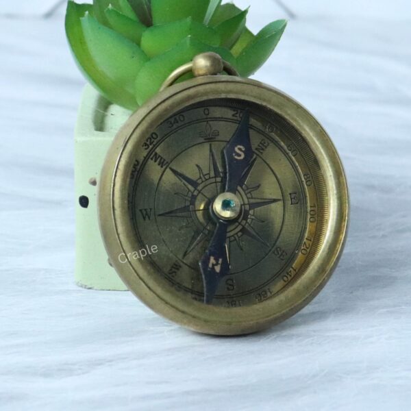 Close-up of the antique brass compass face, showing the intricate details of the compass rose and cardinal points.