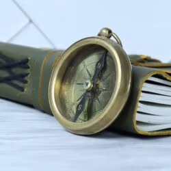 The vintage brass compass resting on a leather-bound journal, symbolizing travel and adventure.