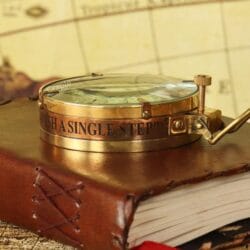 The polished brass Spencer compass resting on a vintage leather book, highlighting the thick glass lens.