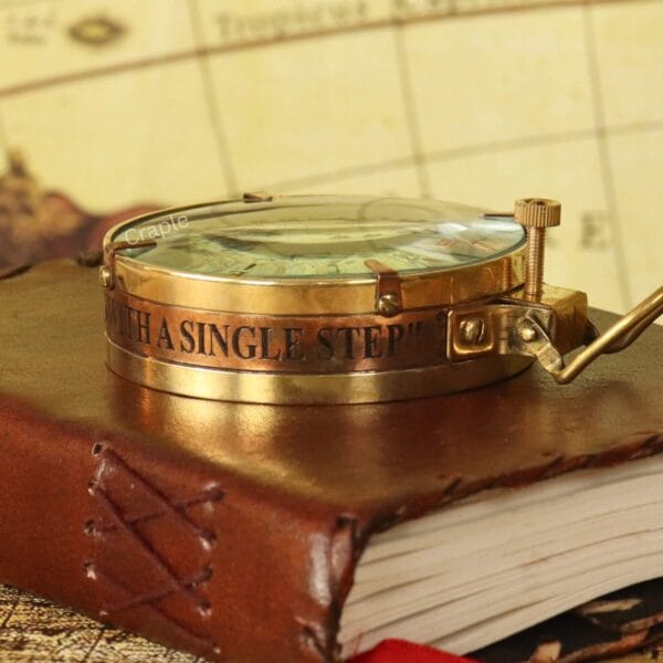The polished brass Spencer compass resting on a vintage leather book, highlighting the thick glass lens.