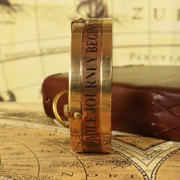 Side view of the brass compass showing the engraved quote 'A SINGLE STEP... THE JOURNEY BEGINS'.