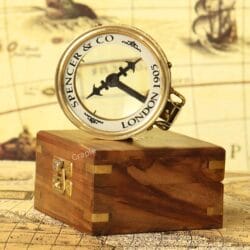 The brass magnifying compass displayed on top of its closed wooden storage box.