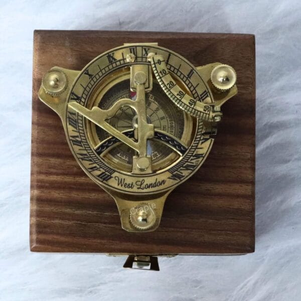 The vintage brass sundial compass mounted on top of its closed wooden display box.