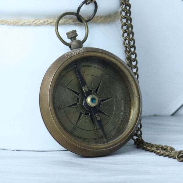 Vintage-style open-face pocket compass in antique brass, with its matching chain partially visible.