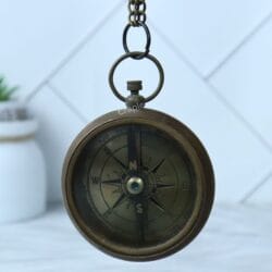 The antique brass pocket compass hanging from its chain loop, showing the full compass face.