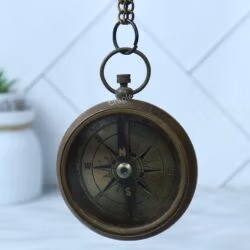 The antique brass pocket compass hanging from its chain loop, showing the full compass face.