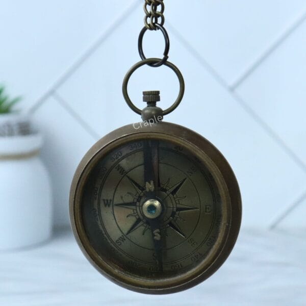 The antique brass pocket compass hanging from its chain loop, showing the full compass face.