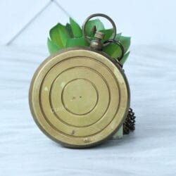 The back of the antique brass pocket compass, showing the smooth, rounded casing and concentric circle details.