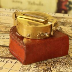 Vintage brass Brunton pocket compass, closed, resting on its brown leather storage case.