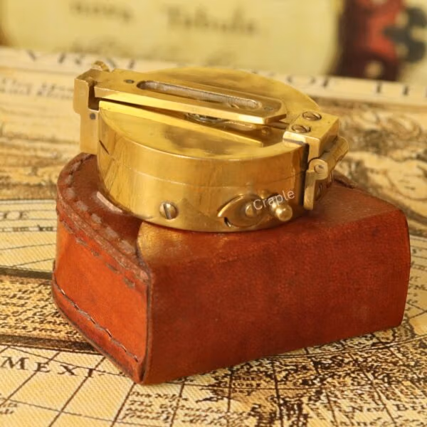 Vintage brass Brunton pocket compass, closed, resting on its brown leather storage case.