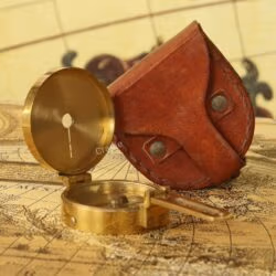 An open brass Brunton compass displayed next to its handcrafted brown leather carrying case.