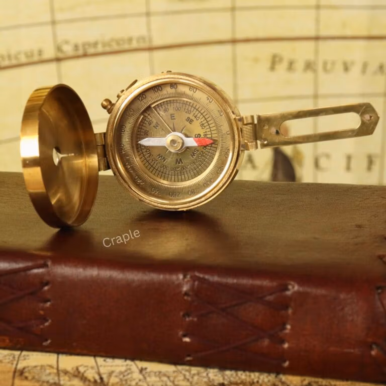 An open, vintage-style brass Brunton compass with its sighting arm extended, showing the detailed navigational dial.