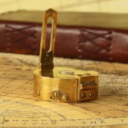 Close-up of the foldable sighting arm and prismatic lens on the vintage brass nautical compass.