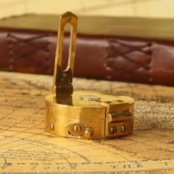 Close-up of the foldable sighting arm and prismatic lens on the vintage brass nautical compass.
